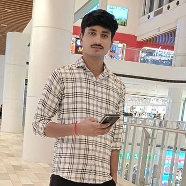Young man in a checkered shirt holding a phone in a shopping mall.
