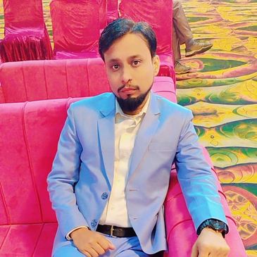 Man in a blue suit sitting on a pink sofa in a colorful carpeted room.
