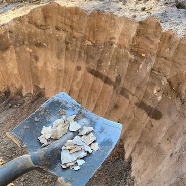 A shovel holding small rocks inside a deep dirt hole.