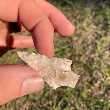 Hand holding a small, pointed arrowhead artifact outdoors.