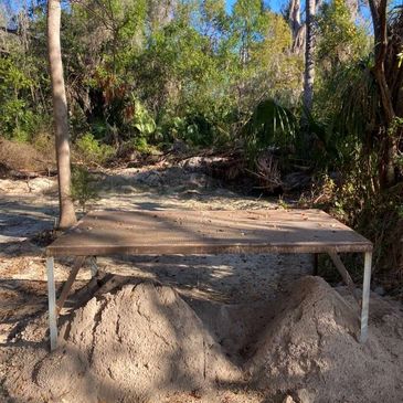 Metal platform supported by sand piles in a wooded area.