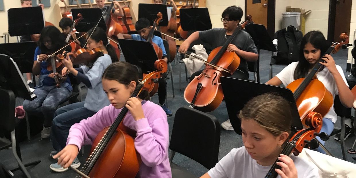 Students playing string instruments in a classroom orchestra setting.