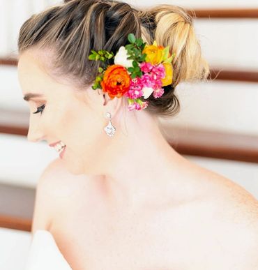 a brown haired bride with orange ranunculus, pink flowers and yellow ranunculus in her hair