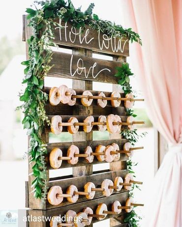 doughnut wall displayed at wedding reception. Wall is decorated with greenery garland