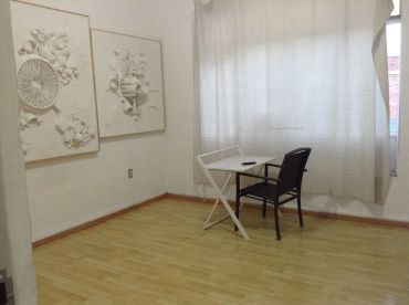 Habitación sencilla con escritorio y silla junto a ventana.