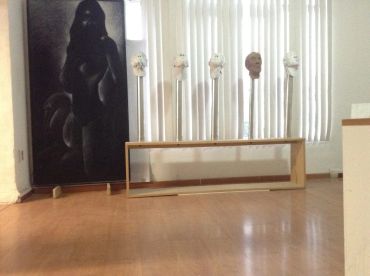 Escultura con cabezas y pintura oscura en habitación luminosa.