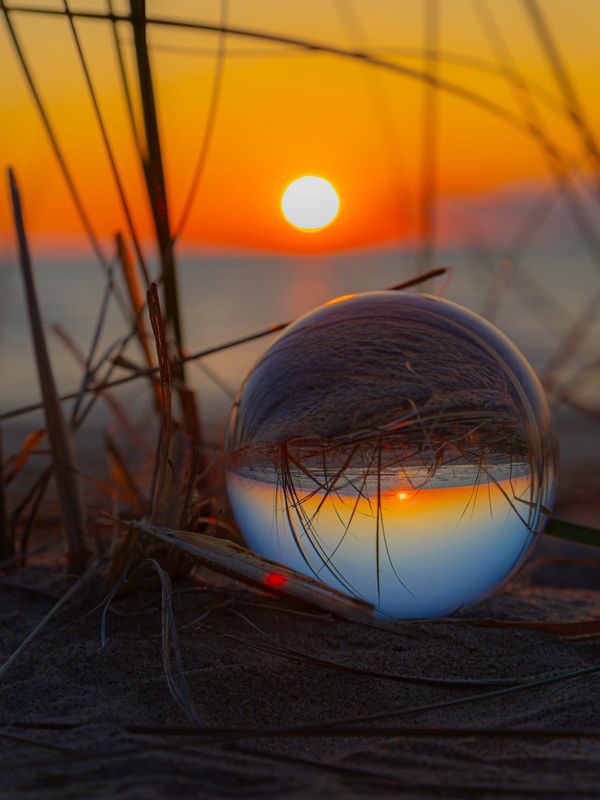Sunset reflected through a crystal ball on beach sand.