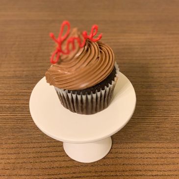 Chocolate cupcake with 'love' topper on white stand.