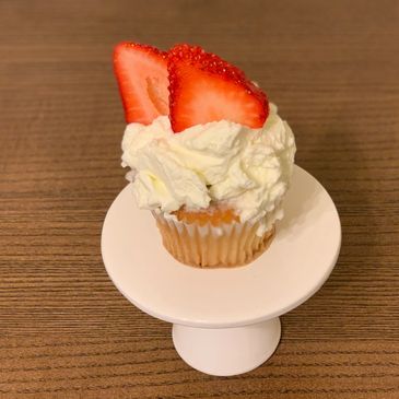 Cupcake topped with whipped cream and fresh strawberry slices on a white pedestal.