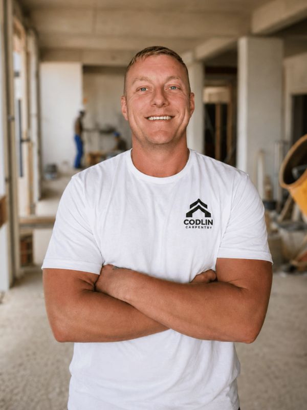 Smiling man in a white Codlin Carpentry t-shirt in a construction site.
