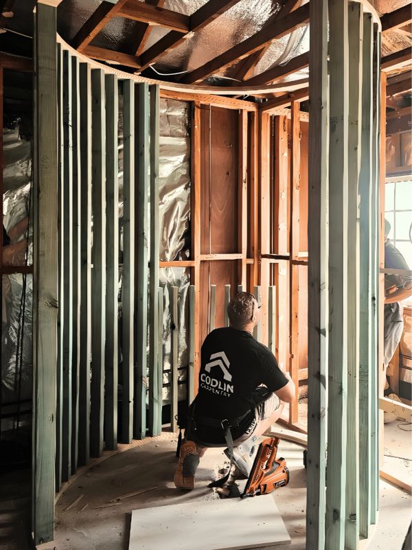 Worker kneeling and building a curved wooden frame indoors.