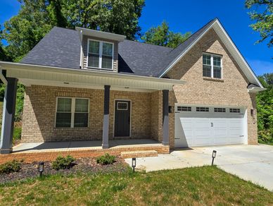 A brick house with a covered porch and two-car garage under a clear blue sky.