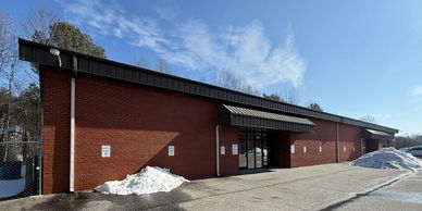A long red brick building with snow piles on each end under a clear blue sky.