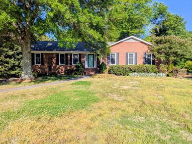 Sunny day view of a brick house with a large front yard and mature trees.