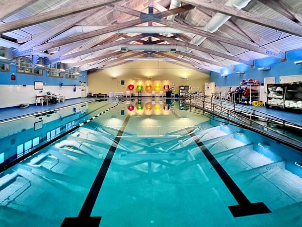 Indoor swimming pool with clear water and lane markers under a wooden beam ceiling.