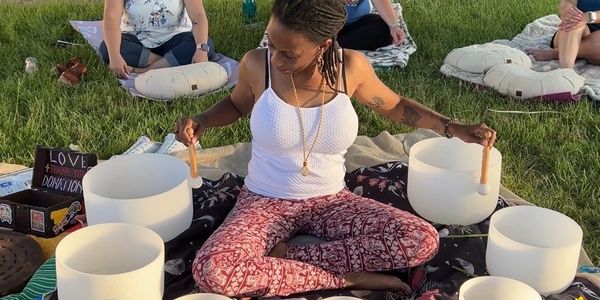 Woman playing singing bowls outdoors on a blanket.