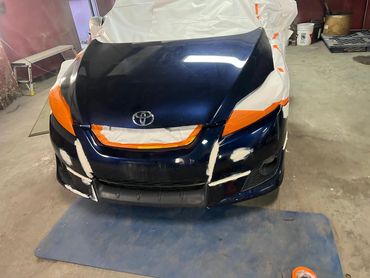 A Toyota car front undergoing paint repair with masking tape and putty applied.