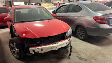 Red car with front damage parked in a garage alongside a gray Mitsubishi.
