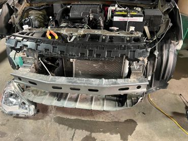 Car front with removed bumper and exposed engine components in a workshop.