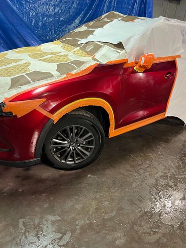 Red car being prepped for painting with masking tape and paper.