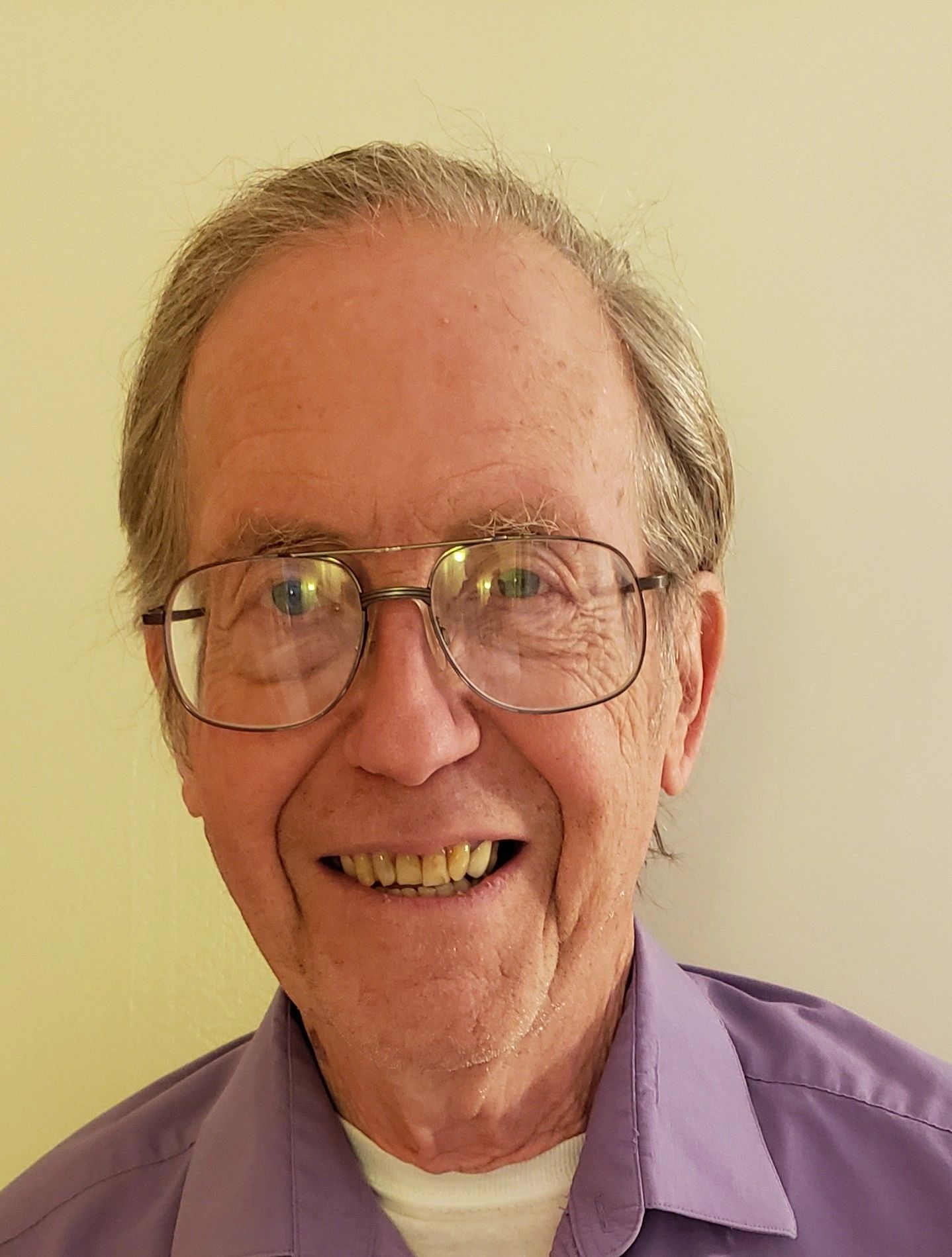Smiling elderly man wearing glasses and a purple shirt.