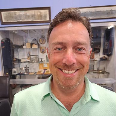 A smiling man in a light green shirt in a room with display cases and framed pictures.