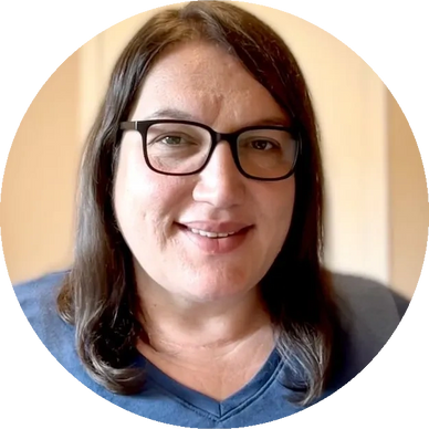 Smiling woman with glasses and shoulder-length hair in a blue top.