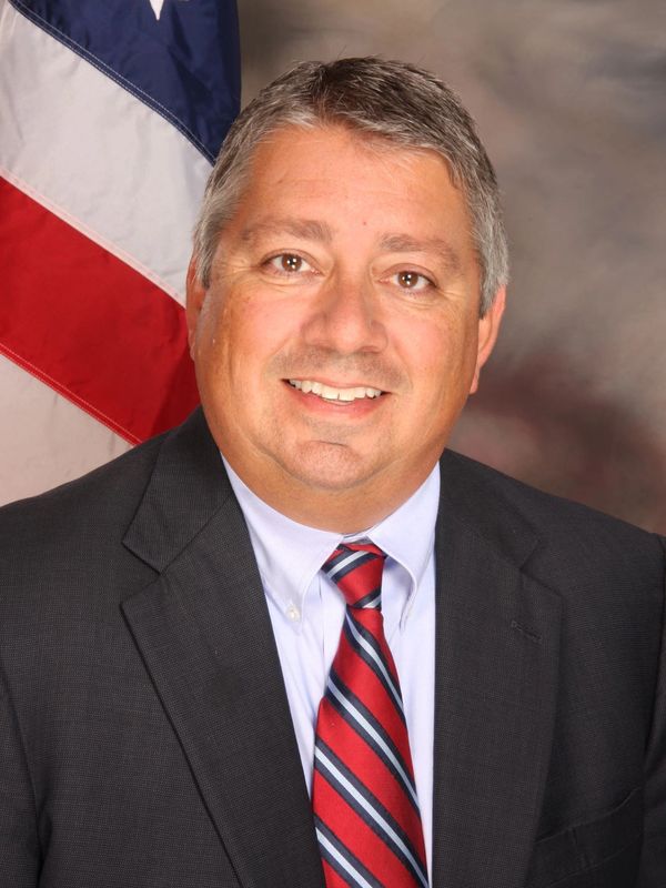Man in suit with American flag background smiling.