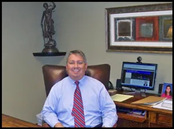 A man in a blue shirt and red striped tie smiling in an office.