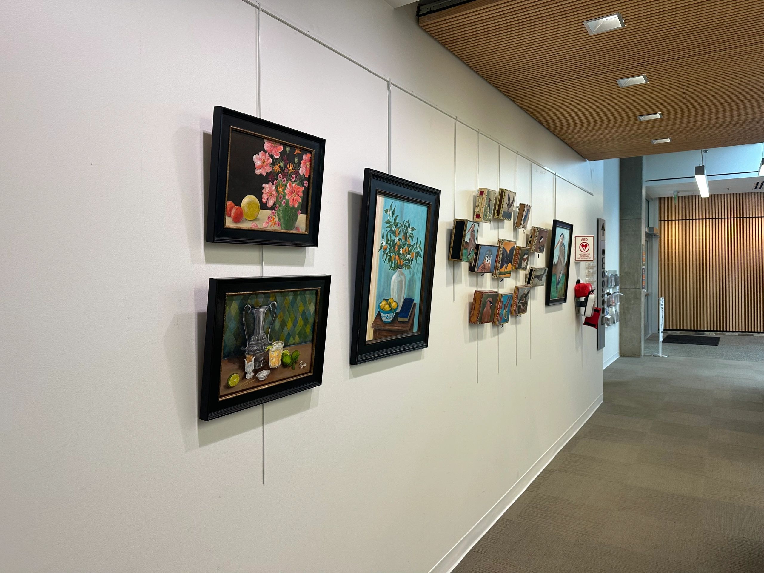 Art gallery hallway with various framed paintings and wooden ceiling.