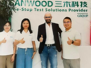 Four people standing in front of a company sign giving thumbs up.