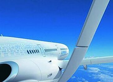 View of an airplane wing and engine flying above clouds under a clear blue sky.