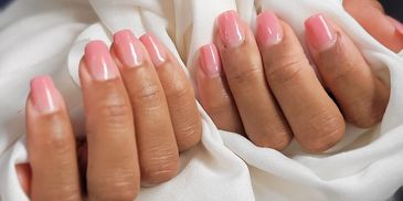 Two hands with manicured nails, one with red polish and the other with pink, holding white fabric.