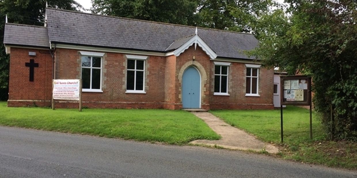 Small brick church building with blue door and cross on lawn.