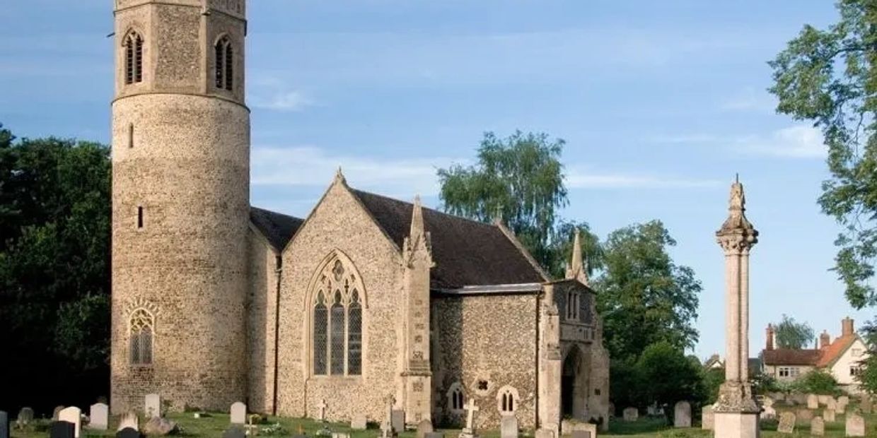 Historic stone church with round tower and cemetery under blue sky.