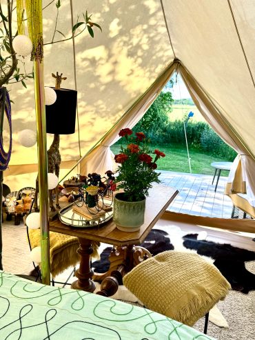 Cozy tent interior with a wooden table, red flowers, and outdoor greenery visible.