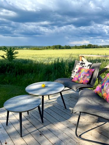 Cozy outdoor seating on a wooden deck with colorful pillows and a scenic field view.