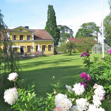 Yellow house with a garden full of blooming white and pink flowers under a clear sky.
