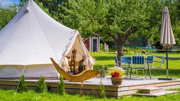 A cozy glamping tent with outdoor seating on a wooden deck in a green garden.