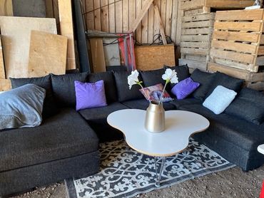 Cozy dark sectional sofa with colorful cushions and a unique white coffee table in a rustic setting.