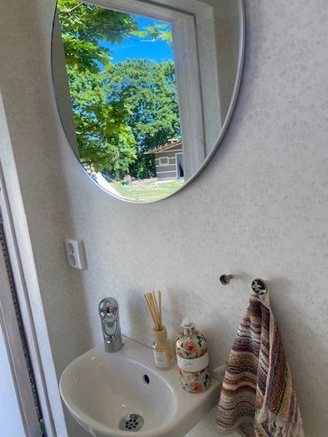 Bathroom sink with a round mirror reflecting a green outdoor scene.
