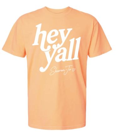 Peach-colored T-shirt with white text saying 'hey y'all' and signed 'Sharon Jo'.