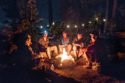 Group of friends sitting around a campfire in the woods at night.