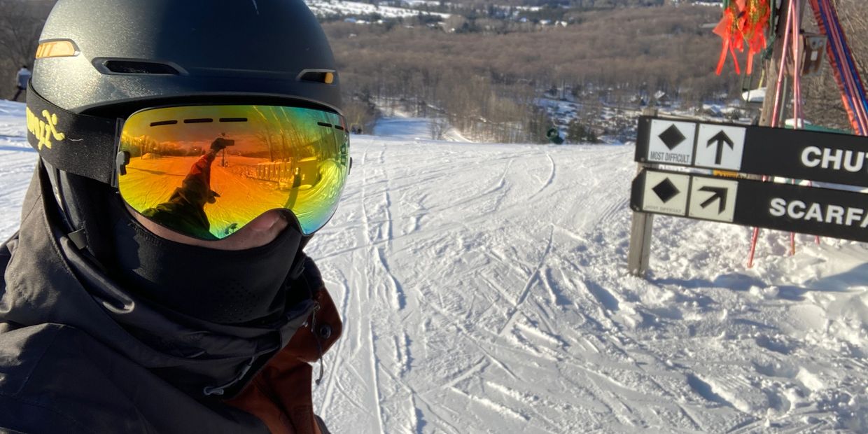 Skier wearing helmet and reflective goggles on a snowy slope with difficulty signs.