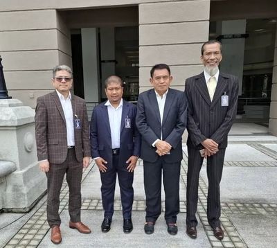 Four men in formal suits standing outside a building for a group photo.