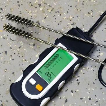 Digital moisture meter with probes and cleaning brushes on a speckled surface.