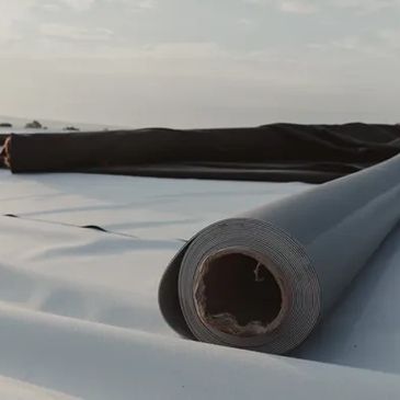 Rolled material spread out on a flat surface under a cloudy sky.