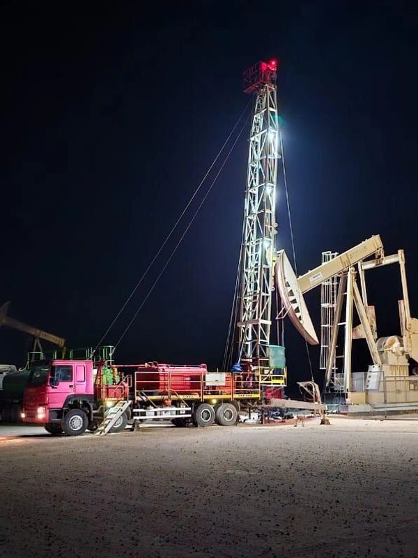 Illuminated oil drilling rig and pumpjack at night in a desert.