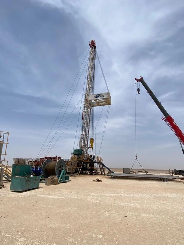 Oil drilling rig operating in a desert under a cloudy sky.