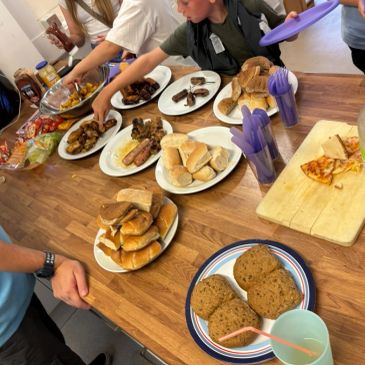 Group serving various foods including bread, pizza, and meat on a table.